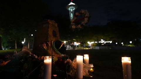 Flowers and candles are seen placed with the Space Needle at background, during the vigil for victims the day after a shooting at Seattle Center during the Bite of Seattle food festival, Monday, July 27, 2026, in Seattle.