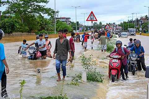 People wade through floodwaters and push two-wheelers along the submerged Jorhat-Sivasagar National Highway near Titabor, in Jorhat district, Assam