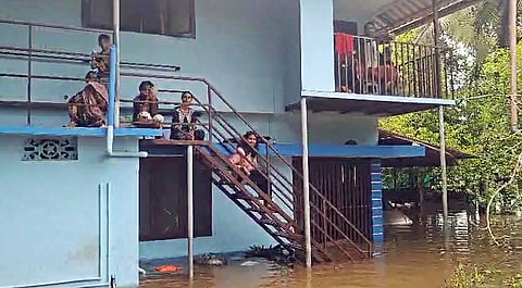 People sit on the staircase of a house submerged in flood water following heavy rainfall, in Pathanamthitta on Sunday.