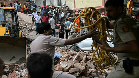 Security personnel cordon off the area as a bulldozer clears debris at the site following a building collapse in the Satya Niketan area in New Delhi on Sunday