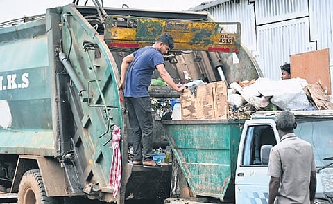 A contract pourakarmika loads waste into a garbage truck without any safety gear.