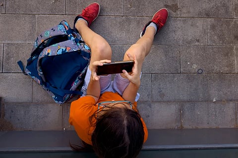 A child plays with his father's phone outside a school in Barcelona, Spain, Monday, June 17, 2024.