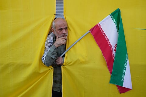 A man holding an Iranian flag peers through an opening in a curtain during the state-organized “Janfada,” or “Sacrifice for Iran,” military-style parade in Tehran, Iran, Friday, Sept. 18, 2026.