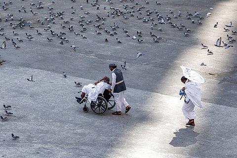 A man pushes a pilgrim in a wheelchair past pigeons feeding outside the Grand Mosque Complex in Saudi Arabia's holy city of Mecca on September 16, 2026.