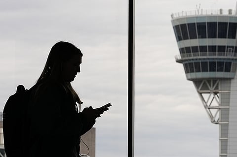 A traveler with a smartphone walks past an air traffic control tower at Philadelphia International Airport in Philadelphia on March 27, 2026