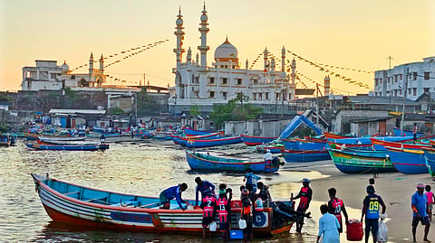 Fishermen prepare to venture into the sea from Vizhinjam harbour in the golden evening light, with the Muhyiddheen Jum'a Masjid in the background.