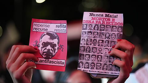 A supporter of Brazilian President Luiz Inácio Lula da Silva, who is running for reelection, holds leaflets that show an image of opposition presidential candidate Flavio Bolsonaro, left, and images of people who disappeared during the military dictatorship, right, at a rally ahead of the presidential runoff election in Sao Paulo, Tuesday, Oct. 13, 2026.