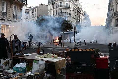 A protester runs through tear gas while a flea market is taking place during clashes between protestors and police officers in Paris, Sunday, Oct. 18, 2026.