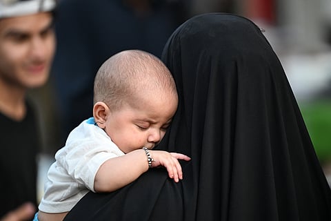 A baby sleeps in a woman's arms at Al-Ashar market in Basra on October 19, 2026.