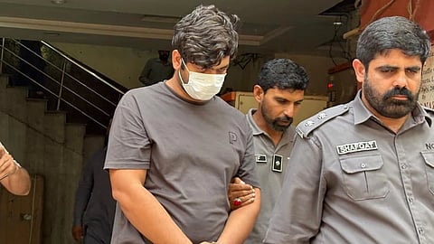 In this photo taken with a smartphone, police officers escort detained suspect Faheem Akram, accused of running an online counterfeit postage operation that U.S. prosecutors say caused more than $126 million in losses to the U.S. Postal Service, in Lahore, Pakistan, Wednesday, Oct. 21, 2026.