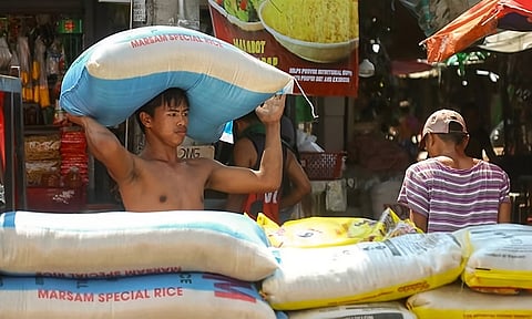 A laborer carries a sack of rice to his employer’s store, as more sacks of rice are waiting to be transferred and arranged in a stall at a public market in Davao City.