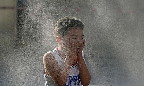 A child reacts to a mist machine as he cools off from the summer heat in Beijing, Saturday, June 15, 2024.