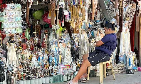 Women sit beside displays of devotional items such as rosaries, crucifixes, and statues of saints outside San Pedro Cathedral in Davao City as Holy Week begins on Palm Sunday, March 29, 2026. They offer religious items to devotees preparing for prayer and reflection.