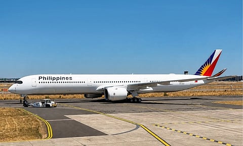 An Airbus A350-1000 aircraft painted in the Philippine Airlines livery sits on the tarmac under a clear blue sky, prepared for towing by a ground handling vehicle.
