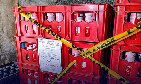 Red plastic crates filled with impounded liquefied petroleum gas (LPG) canisters and cylinders sit wrapped in yellow caution tape following a joint enforcement operation by the Department of Energy Mindanao Field Office (DOE-MFO) at the Bankerohan Public Market. Officials seized the items for direct violations of Republic Act 11592 (LPG Industry Regulation Act), targeting the illegal distribution and refilling of uncertified portable cartridges.