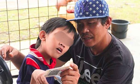 A father and his child review an official document during a Department of Social Welfare and Development (DSWD) payout event in Davao del Sur. The activity is part of the agency's Project Aruga, an initiative providing a ₱2,000 monthly stipend to children with developmental disabilities to assist with medical and daily care expenses.