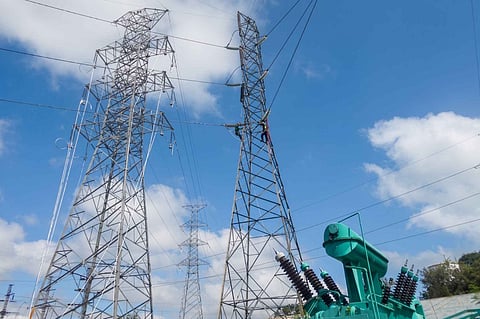 convert this to news-wire style photo captionWorkers perform maintenance tasks on a lattice transmission tower near a substation transformer, under a partly cloudy sky, September 16, 2026.