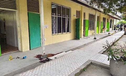 Evidence markers and a pool of blood line an outdoor hallway at Banga National High School on Saturday, following a deadly school shooting the previous day. A 14-to-16-year-old Grade 9 student opened fire with a 9mm pistol belonging to his father, a Department of Education employee, killing three people and wounding several others before taking his own life. Authorities revealed the suspect bypassed a home vault to access the weapon and had active digital footprints on the deep dark web, sparking national calls for stricter gun controls and school safety reforms.