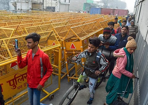 किसानों को रोकने के लिए लगाए गए बैरिकेड्स के किनारों से मुश्किल से निकलते आम लोग