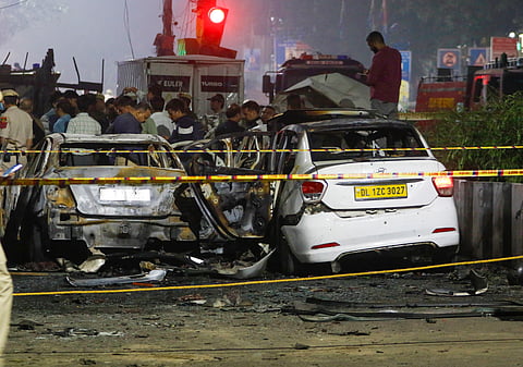 Police personnel stand near the charred remains of vehicles at the site of a car blast near Gate No. 1 of the Red Fort Metro Station, in New Delhi.