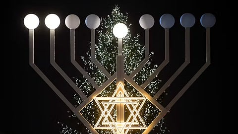 Candles on a large Hanukkah menorah shine in front of a Christmas tree at the Brandenburg Gate in Berlin, Germany, in 2015.