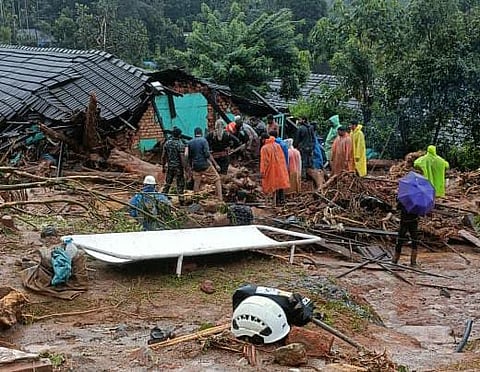 People surrounded by debris inspect a collapsed house after a landslide.
