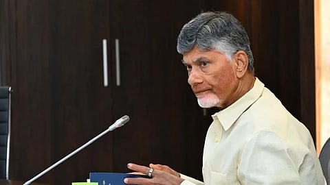 Andhra Pradesh CM Chandrababu Naidu sitting at a desk in side profile looking to his left with his hands opening a thin blue book