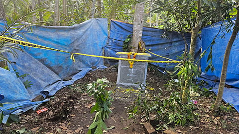 Gopan Swami's Samadhi, adorned with a garland, cordoned off with yellow tape amidst trees and greenery.