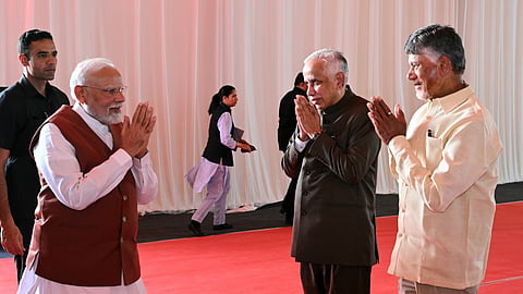 Indian Prime Minister Narendra Modi greets Andhra Pradesh Governor S. Abdul Nazeer and TDP leader N. Chandrababu Naidu with folded hands in a traditional gesture (namaste) at a formal event, standing on a red carpet with a white curtain backdrop.