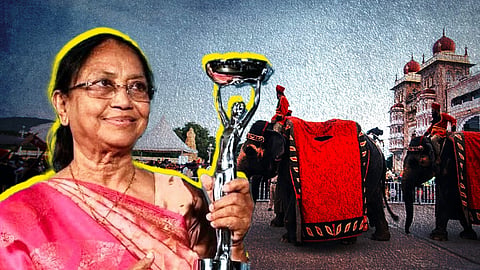 A woman in a pink sari holding a trophy. In the background is a man riding an elephant in front of the Mysore Palace.