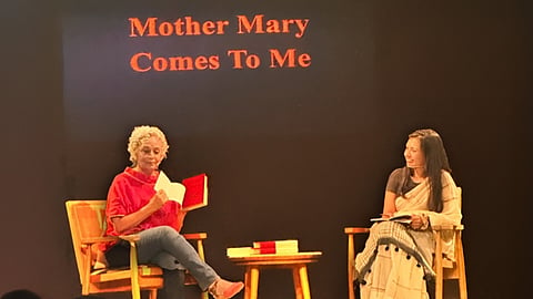 Arundhati Roy is seated on a chair on the stage, holding a copy of the memoir, along with Manasi Subramanian, editor, Penguin India.