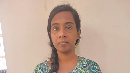A woman standing indoors against a light-colored wall, wearing a green and blue printed kurta with her hair tied in a side braid, looking at the camera with a neutral expression.