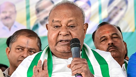 Former prime minister HD Deve Gowda seated on a chair at a stage, speaking with a mic held in his left hand
