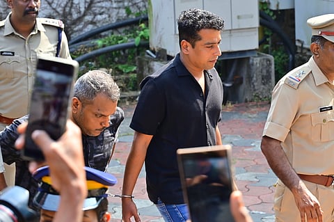 Pulsar Suni in handcuffs, escorted by Kerala Police officers as he is brought to court for the verdict in the 2017 Malayalam actor assault case, with photographers capturing the scene.