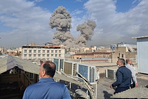People watch as smoke rises on the skyline after an explosion in Tehran, Iran, Saturday, Feb. 28, 2026.
