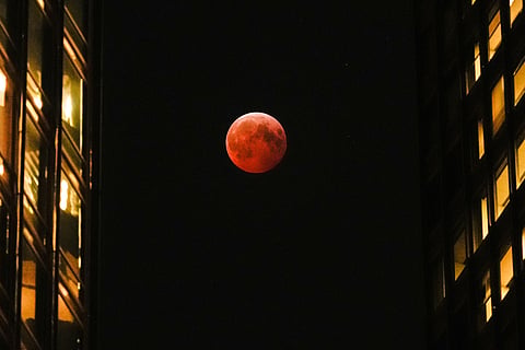A total lunar eclipse, known as the blood moon, is visible between skyscrapers Friday, March 14, 2025, in downtown Chicago.