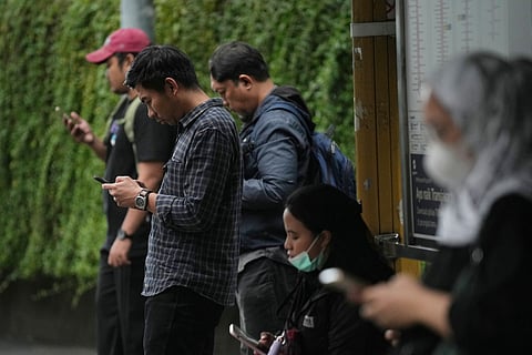 People use their mobile phones at a bus stop in Jakarta, Indonesia, Friday, March 6, 2026.