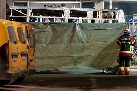 Firefighters and police officers install barriers to secure the area where a postal bus caught fire in Kerzers, Switzerland, Tuesday, March 10, 2026, after several passengers were killed and others injured when a postal bus caught fire late Tuesday afternoon in the center of Kerzers, according to the Fribourg cantonal police.