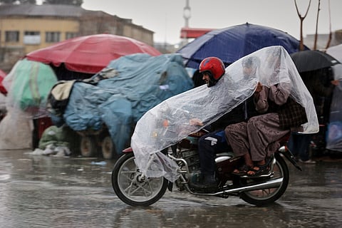 A man rides a motorcycle with two passengers under a plastic cover through heavy rain in Kabul, Afghanistan, Tuesday, March 31, 2026.