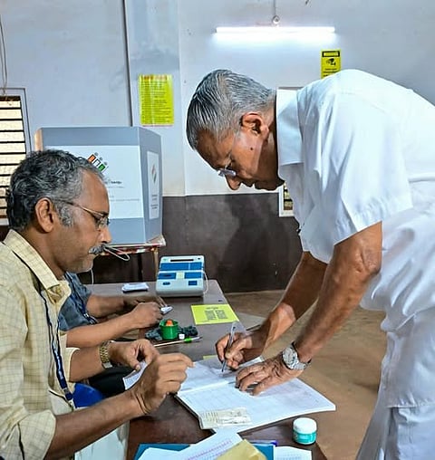 Pinarayi Vijayan bending at a desk in the polling booth to sign his name against the electoral roll.