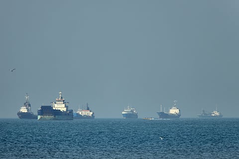 Cargo ships, including bulk carriers and general cargo vessels, sit at anchor offshore as a small motorboat passes in the foreground, in the Strait of Hormuz off Bandar Abbas, Iran, Monday, May 4 , 2026.