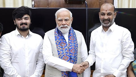 Bandi Bhageerath, Narendra Modi, Bandi Sanjay stand together, posing for a photo. Modi and Sanjay shaking hands. Bhageerath and Sanjay in white shirts, Modi wears a blue scarf
