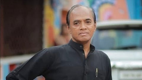 Writer and translator DI Aravindan in a black kurta leaning against a red-coloured vehicle