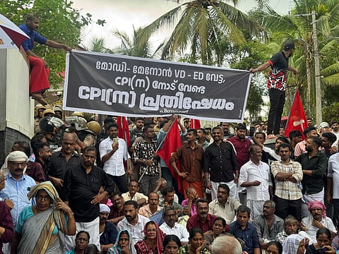 CPI(M) stages a sit-in protest on the road in front of Pinarayi Vijayan’s residence at Pinarayi in Kannur. A black and white banner and the cpim's red flags visible