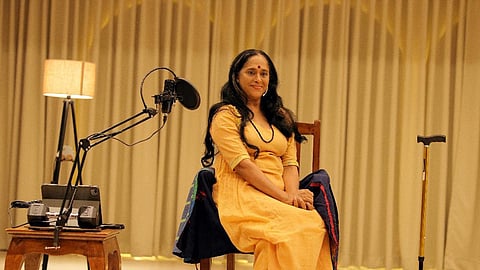 Sajitha Madathil sitting on a chair with a mic before her, during the performance