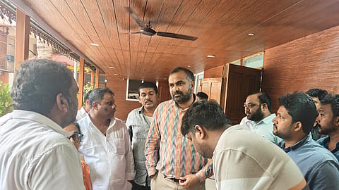 A group of official-looking men gather around a table under a wooden ceiling, reviewing and signing documents during an inspection.