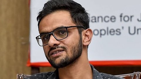 Umar Khalid seated at a press conference table, speaking into a microphone.