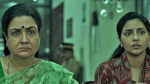 Urvashi, Aishwarya Lekshmi in a scene from Aasha, seated next to each other and looking towards the screen
