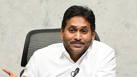 Former Chief Minister of Andhra Pradesh, Y. S. Jagan Mohan Reddy, seated at a desk in a white shirt, gesturing with his hand while speaking into multiple news organization microphones during a press conference.