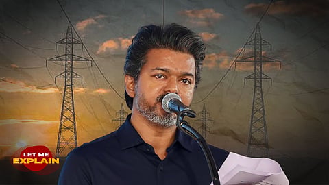 Tamil actor and politician Vijay speaking at a microphone, set against a background of high-voltage power transmission towers at sunset with a "Let Me Explain" logo.